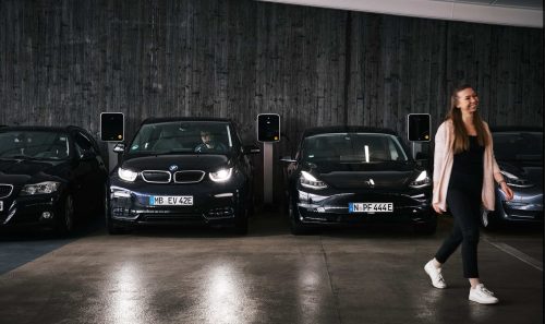 In einer Gewerbeimmobilie werden Elektrofahrzeuge an Ladesäulen geladen. Eine glückliche Kunden verlässt ihr eAuto und lässt es bequem während dem Parken laden.